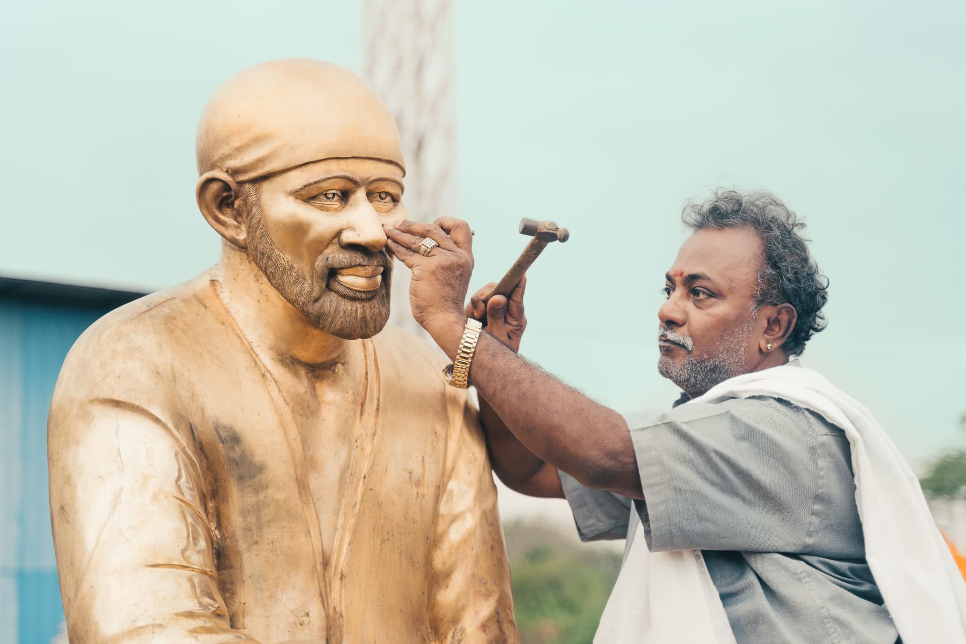 Sthapathy R. Ravindran chasing the face of a monumental Sai Baba figure with hammer and chisel
